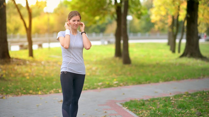 The athlete is training in the park at dawn. The athlete runs along the track, listens to music with headphones. Healthy lifestyle.