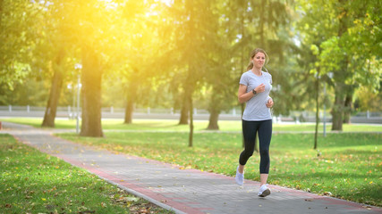 The athlete is training in the park at dawn. The athlete runs along the track, listens to music with headphones. Healthy lifestyle.