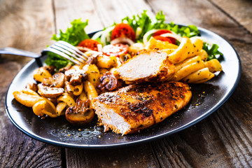 Roast chicken breast with pasta and vegetables on wooden background