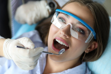Girl feels comfortable at dental examination. Routine check-up includes complete dental cleaning by dentist. Using special tools, an specialist removes deposits, including plaque and stone.