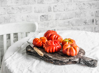 Fresh heirloom ripe tomatoes on rustic cutting board to light the kitchen table on a light...