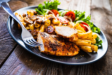 Roast chicken breast with pasta and vegetables on wooden background