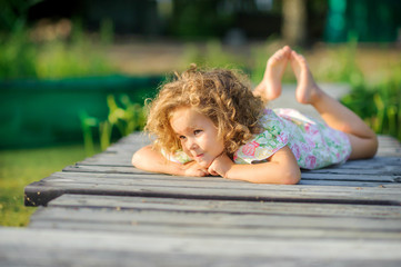 Cute girl lies and rests on a wooden pier on the river. Children have a rest outdoors. Childhood.