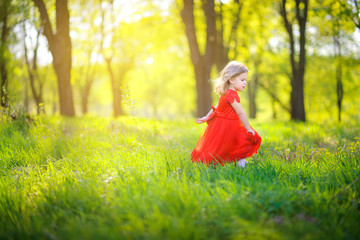 Cute girl in a red dress walks in a beautiful spring park. Children relax and walk outdoors. Childhood.