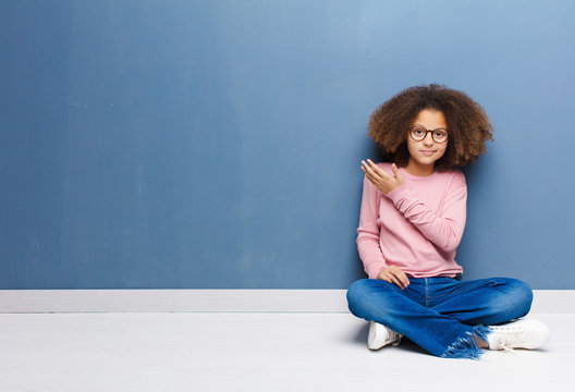 african american little girl feeling confused and clueless, wondering about a doubtful explanation or thought sitting on the floor