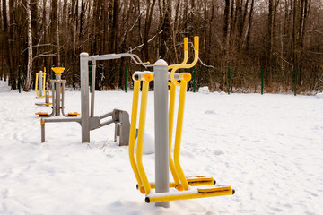 Grey and yellow simulators at sports ground on snow in park on natural winter trees background.