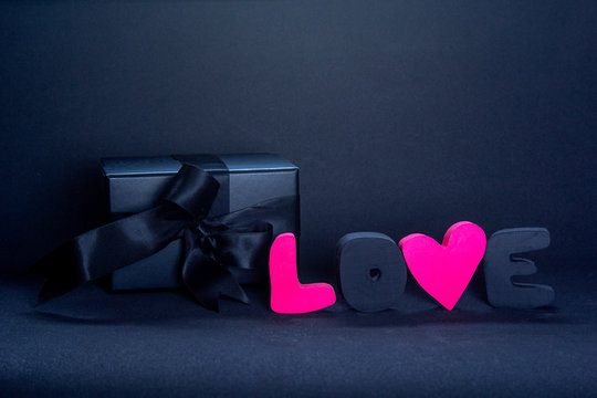 Black gift box and red letters LOVE on dark background, copy space. Valentine's day, birthday romantic concept, greeting card.