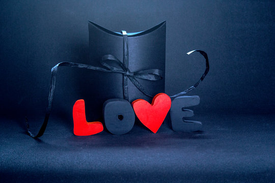 Black gift box and red letters LOVE on dark background, copy space. Valentine's day, birthday romantic concept, greeting card.