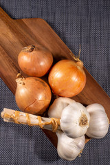 unpeeled onions and garlic on a kitchen cutting board. Vertical shot. View from the top.
