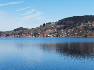 Fototapeta na wymiar Schliersee in Oberbayern. Ort am Horizont mit lichtreflexion im Winter und Kirchdorf Sankt Sixtus 