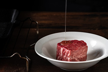 Raw filet Mignon steak in a white plate is poured with olive oil before grilling