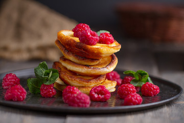 Pancakes with raspberries on a black and wooden background.