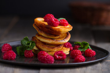 Pancakes with raspberries on a black and wooden background.