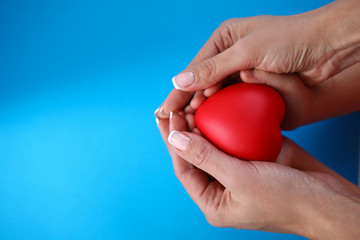 Maternal care for health child, heart in hands. Close-up mother hands holding small heart and hands child in palms on blue background. Black sign is drawn on heart. Maternal devotion and childcare.
