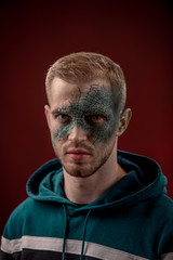 man with professional horror movie make-up green lizard on dark red background. lizard eye