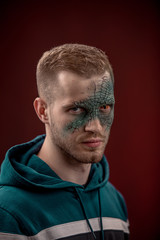 man with professional horror movie make-up green lizard on dark red background. lizard eye