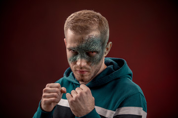 man with professional horror movie make-up green lizard on dark red background. lizard eye