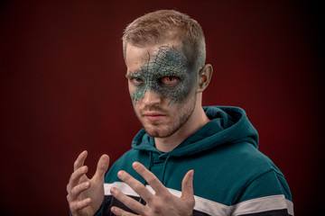 man with professional horror movie make-up green lizard on dark red background. lizard eye