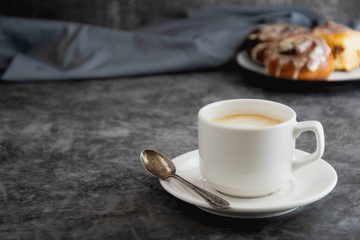 Cup of black coffee and cinnamon roll, cinnabons on background. Dark board, copy space.