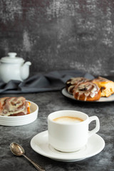 Cup of black coffee and cinnamon roll, cinnabons on background. Dark board, copy space.