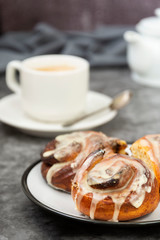 Cinnamon danish bun or cinnabons on dark background with coffee cup. Sweet homemade pastry.