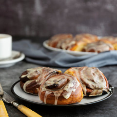 Cinnamon danish bun or cinnabons on dark background with coffee cup. Sweet homemade pastry. Square image.