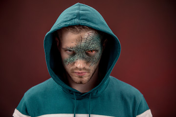 man with professional horror movie make-up green lizard on dark red background. lizard eye