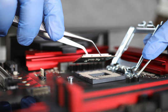 Manual assembly and repair mechanical device. Hands in blue gloves hold tongs. Technician collects metal parts and mounts them on device lying on table. Small parts are attached with tweezers.