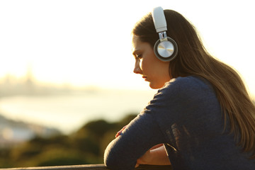 Sad pensive woman listening to music at sunset