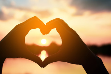 Fototapeta premium Beautiful Silhouette hand made heart shape on the sunset background.