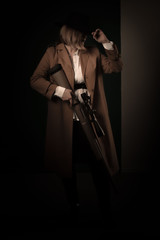 Retro gangster woman in a brown cloak and black hat with airguns in hands. Photoshoot in the style...