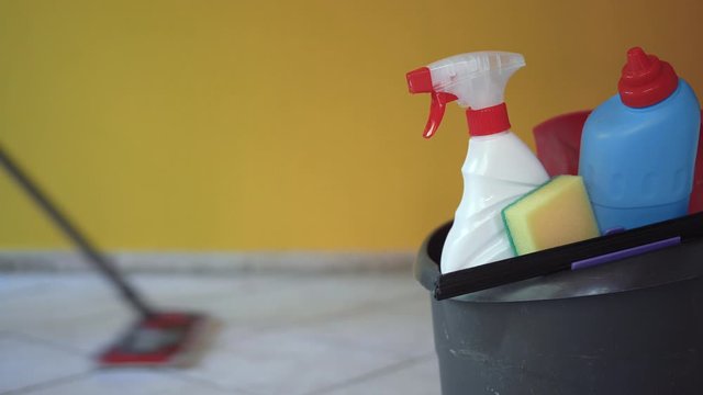 House spring cleaning items or supplies in a bucket. Caucasian man washing tile floor with a mop in a background.