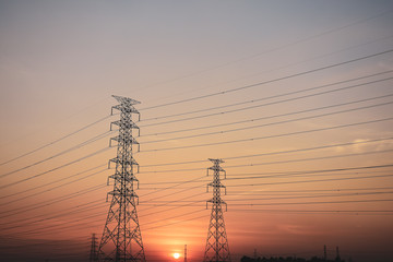 Silhouette High voltage electric tower line in cornfield at sunset.