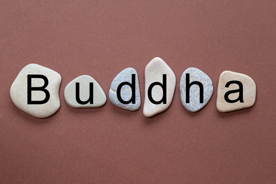 Buddha as a word on flat stones in natural color and shape. A letter in black color on each stone isolated against a brown background