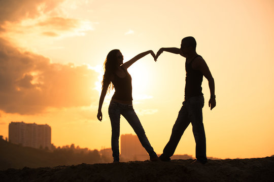 Silhouette of couple on a sunset making heart symbol