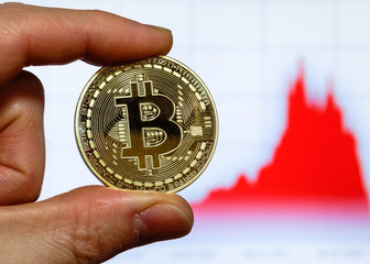 Bitcoin cryptocurrency coin in front of a computer screen with bitcoin chart
