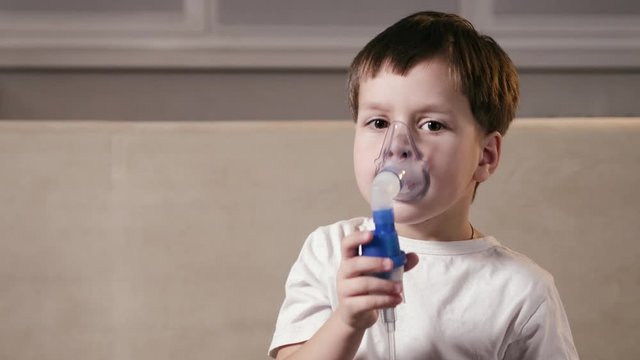 Cute funny boy breathes deeply through a nebulizer mask with medication to treat an infection. Inhalation the lungs of people in the home. Concept of medicine and health