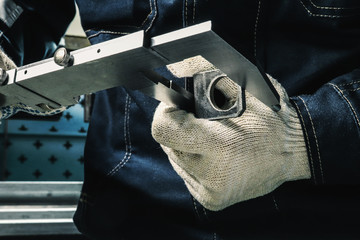 A worker measures a part with a caliper measuring tool at a factory. Worker works in a factory
