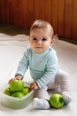 Fototapeta premium Beautiful smiling girl is sitting on a white plaid with plastic container with green apples.