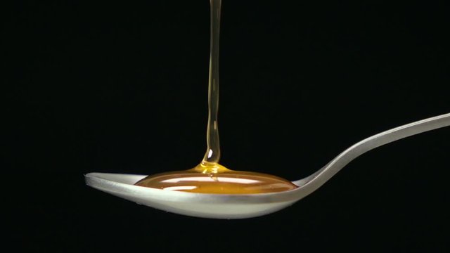 Slow motion shot : Close up honey dripping on the stainless tea spoon on black back ground.