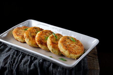 Appetizer syrniki, cottage cheese pancakes, on the white ceramic platter against the black background