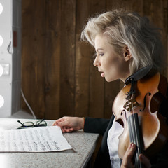 Young blonde woman violinist reads notes before a performance