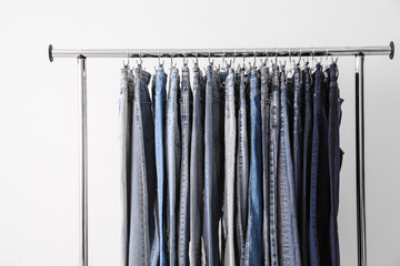 Rack with different jeans on light background