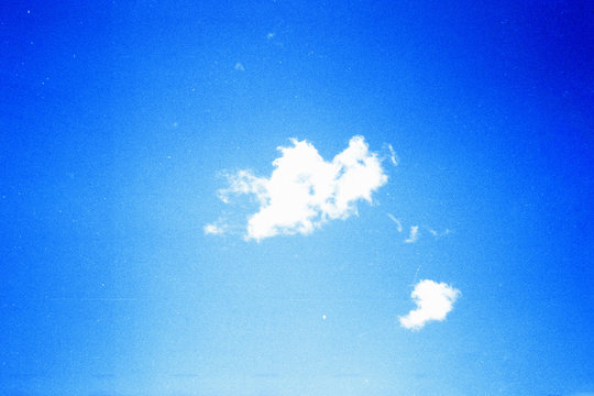 Grunge image of blue sky with a cloud on grainy film texture