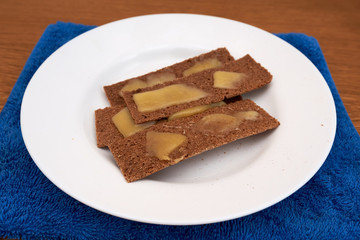 Dietary simple toasts dark bread crisps topped with melted cheese on a white round plate on a blue towel on a wooden table. home cooking