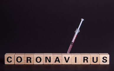 wooden cubes with text coronavirus and a syringe, vaccine, black background