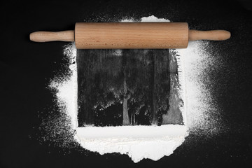 Flour and rolling pin on black table, flat lay