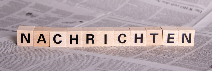 German text Nachrichten, what means news, on wooden cubes, newspaper as background