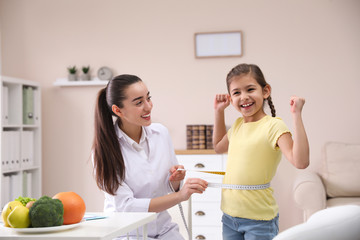 Professional nutritionist measuring waist of little girl in office