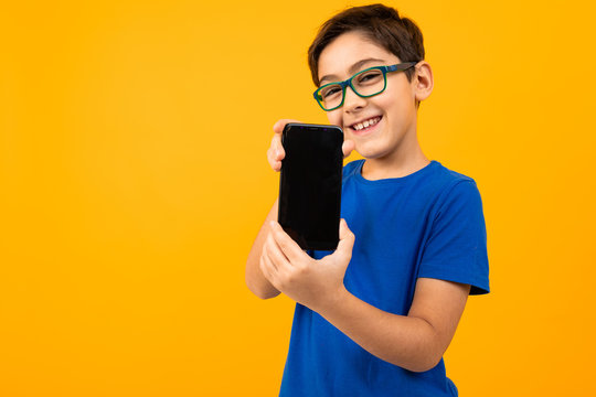 cute boy in glasses and a blue t-shirt holds the phone with the screen forward with a layout on a yellow background with copy space